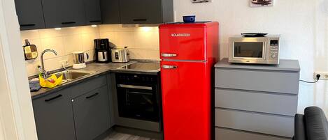 A compact kitchen with dark cabinets, a red refrigerator, a microwave, and a coffee maker.
