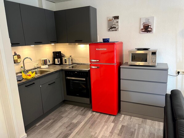 A compact kitchen with dark cabinets, a red refrigerator, a microwave, and a coffee maker.