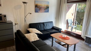 Una sala moderna con un sofá de cuero negro, una mesita de madera y una lámpara de pie. En la pared, un cuadro que representa una escena de playa.