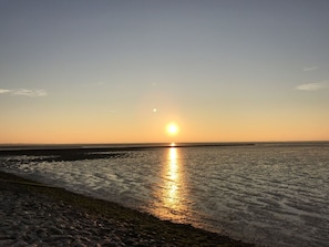 A beach with the sun reflecting on the water at sunset.