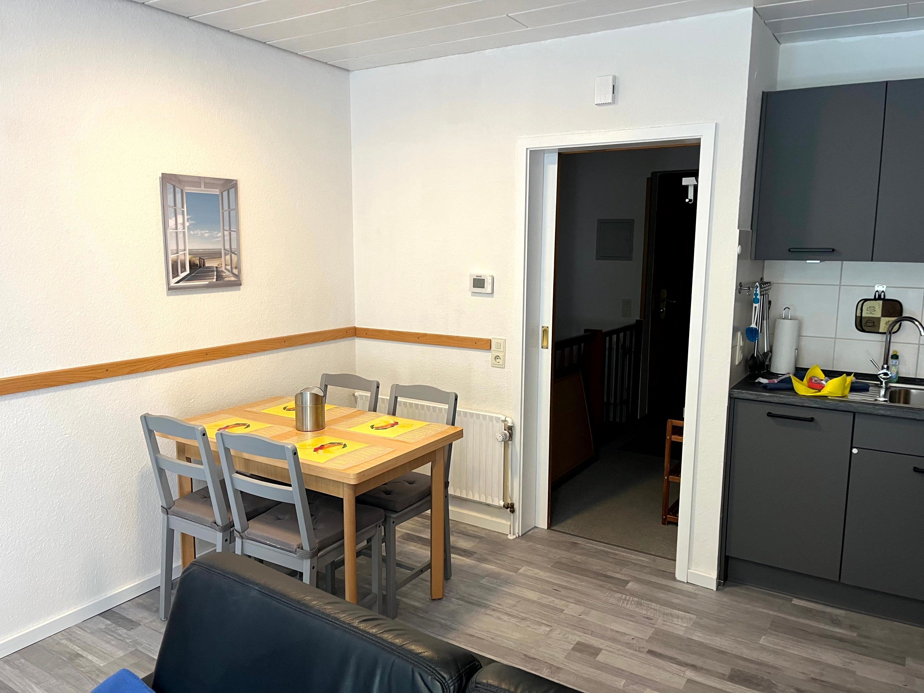 Un coin repas avec une table et des chaises en bois, un radiateur, et une cuisine équipée d’armoires et d’un évier.