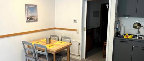 Un coin repas avec une table et des chaises en bois, un radiateur, et une cuisine équipée d’armoires et d’un évier.