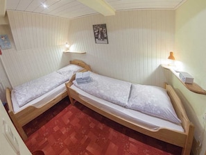 Ein Zimmer mit zwei Holzbetten, einem roten Teppich mit Muster und einem kleinen Tisch mit einer Lampe.