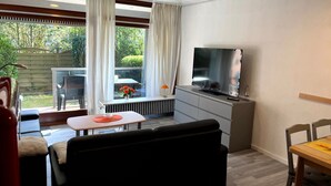 Una sala de estar con televisor, sofá y mesa de comedor.