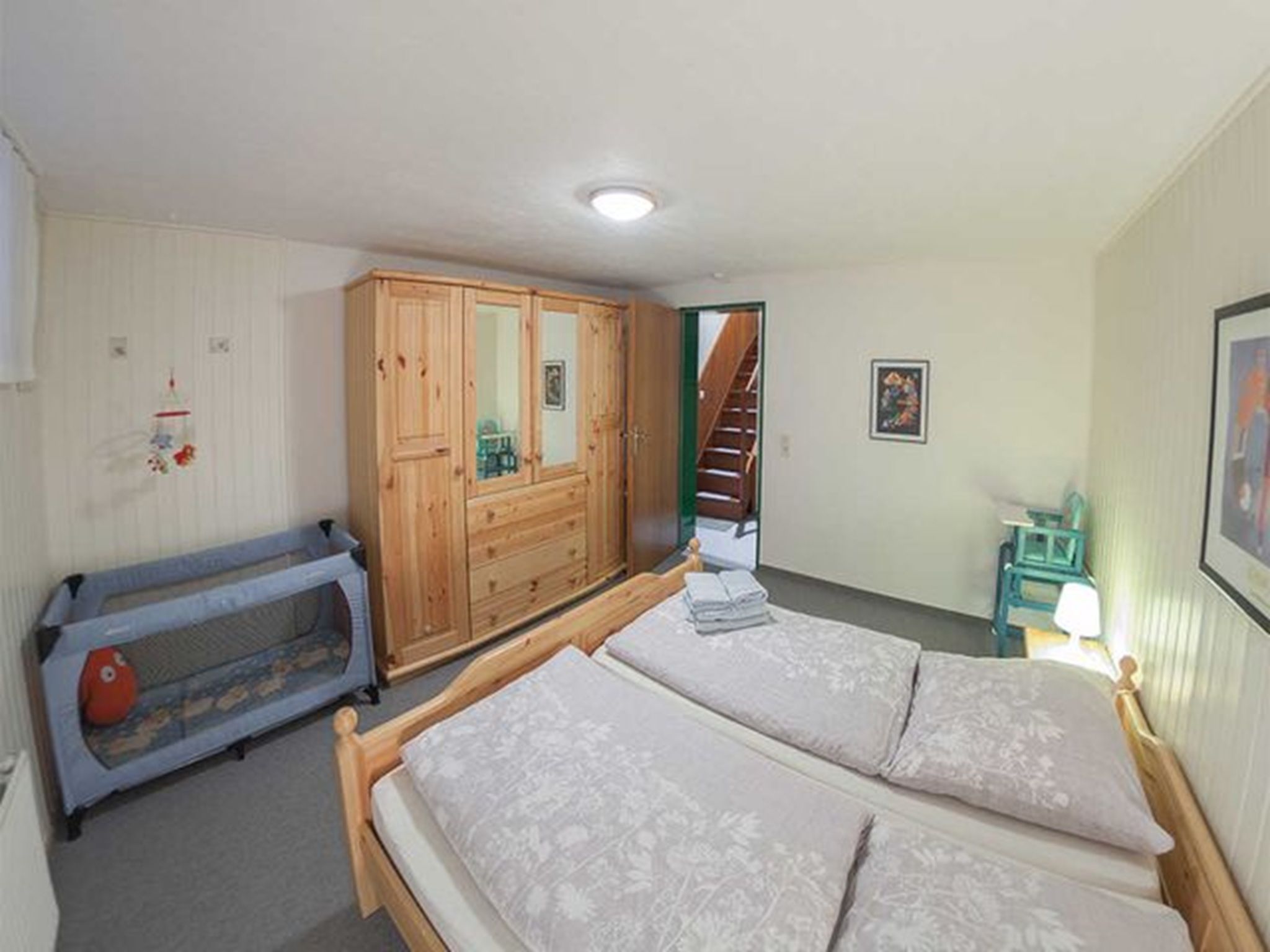 A bedroom with a double bed, a wooden wardrobe, a small table, and a crib.