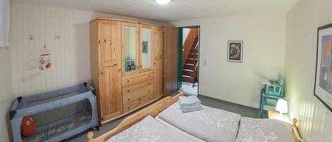 A bedroom with a double bed, a wooden wardrobe, a small table, and a crib.