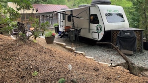 Una casa rodante con un letrero que dice 'NO BOUNDARIES', una parrilla cubierta y una zona de patio con asientos exteriores.