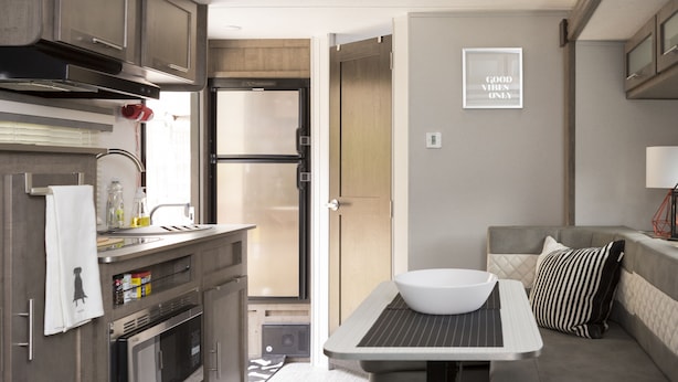 Una cocina moderna con horno empotrado, lavadero y refrigerador. Hay un pequeño comedor con una mesa y un tazón.