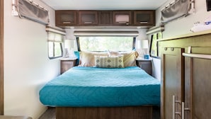 Dormitorio compacto en una caravana, con cama, mesitas de noche y armarios.