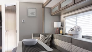 Una cocina moderna con una mesa de comedor, un bol, y un banco. Hay una ventana con persianas y una cita enmarcada en la pared.