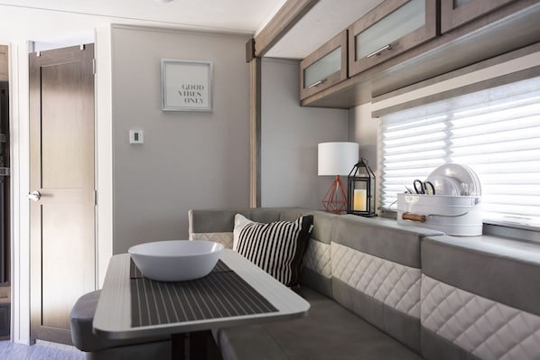A modern kitchen with a dining table, a bowl, and a bench. There is a window with blinds and a framed quote on the wall.