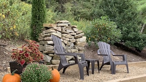 Un jardín con sillas Adirondack, un muro de piedra y una terraza de madera.