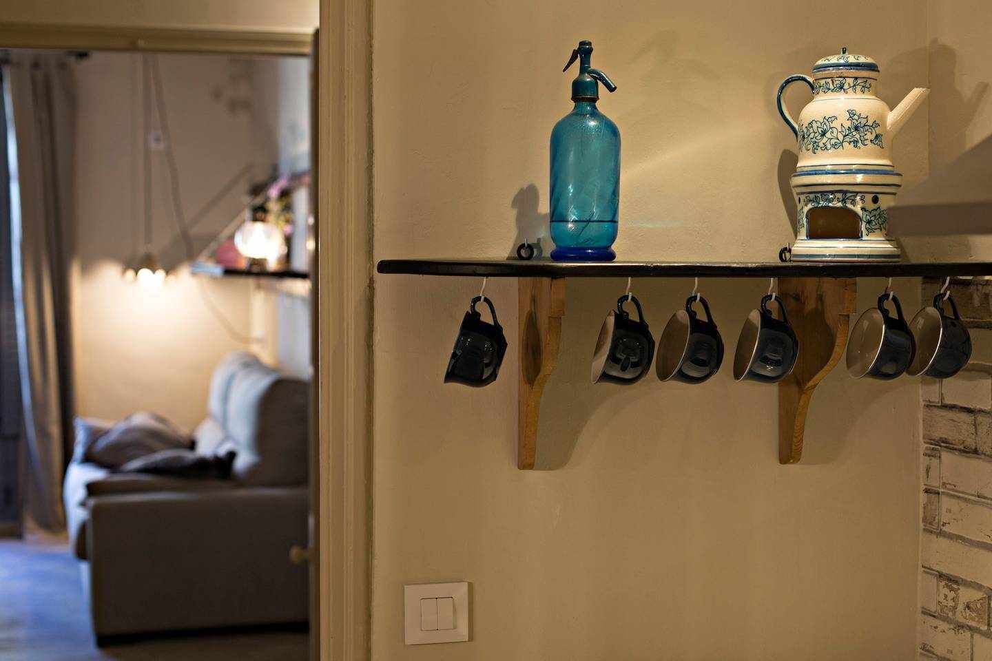 A kitchen with a shelf holding a blue spray bottle, a decorative teapot, and hanging pots.