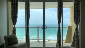 Une chambre avec un lit, une chaise et une vue sur l’océan, grâce à de grandes portes vitrées.