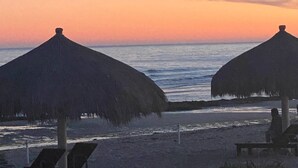Une plage avec deux parasols en chaume et un banc.