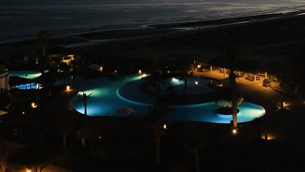 Un complexe hôtelier doté d’une grande piscine illuminée et offrant une vue sur l’océan au crépuscule.