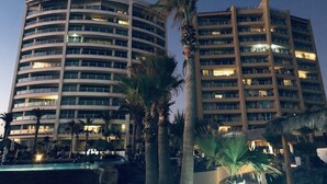 Un hôtel à plusieurs étages, doté d’une façade incurvée, d’une piscine extérieure et de palmiers.