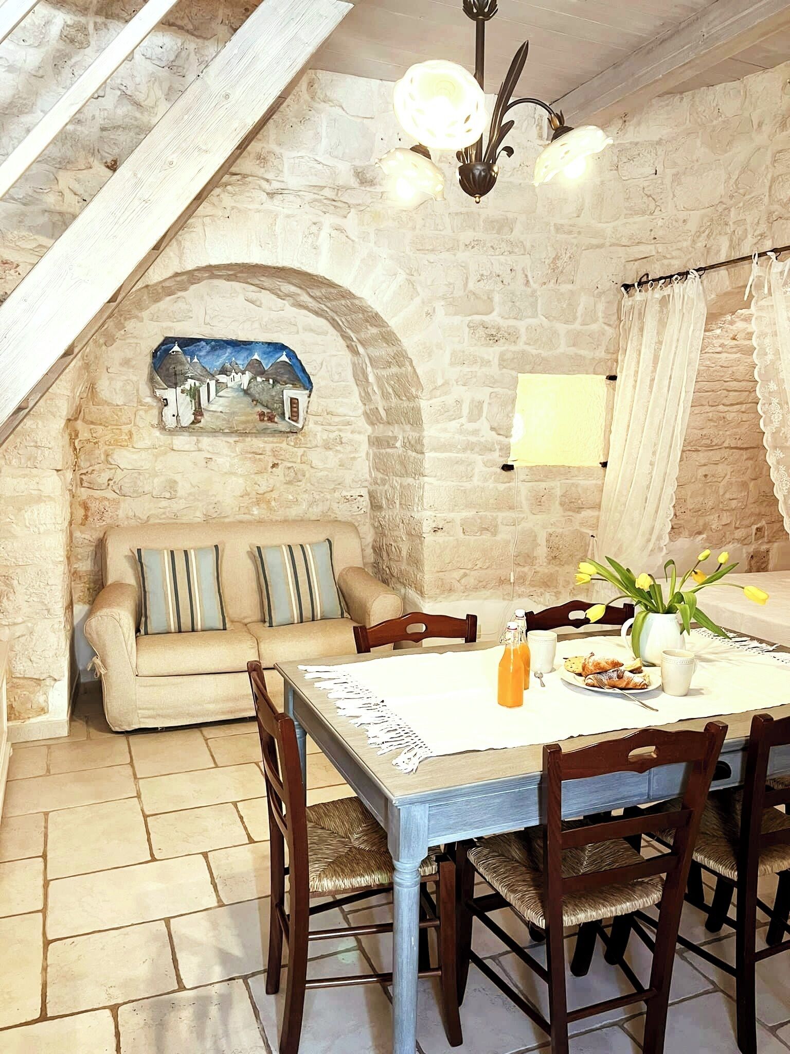 A cozy dining area with a stone wall, a wooden ceiling, and a rustic table set for breakfast.