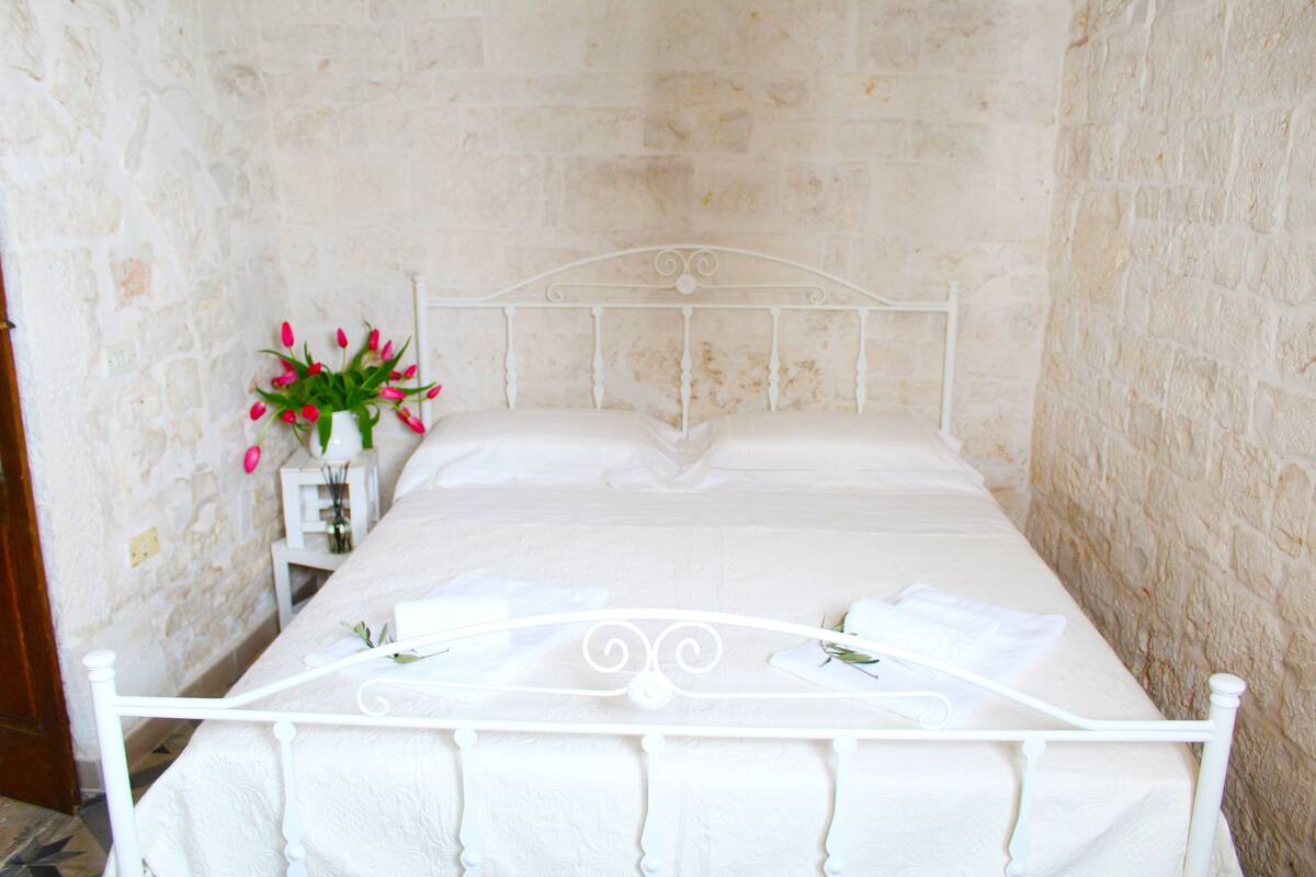 Una cama bien hecha con sábanas blancas en una habitación con paredes de piedra.