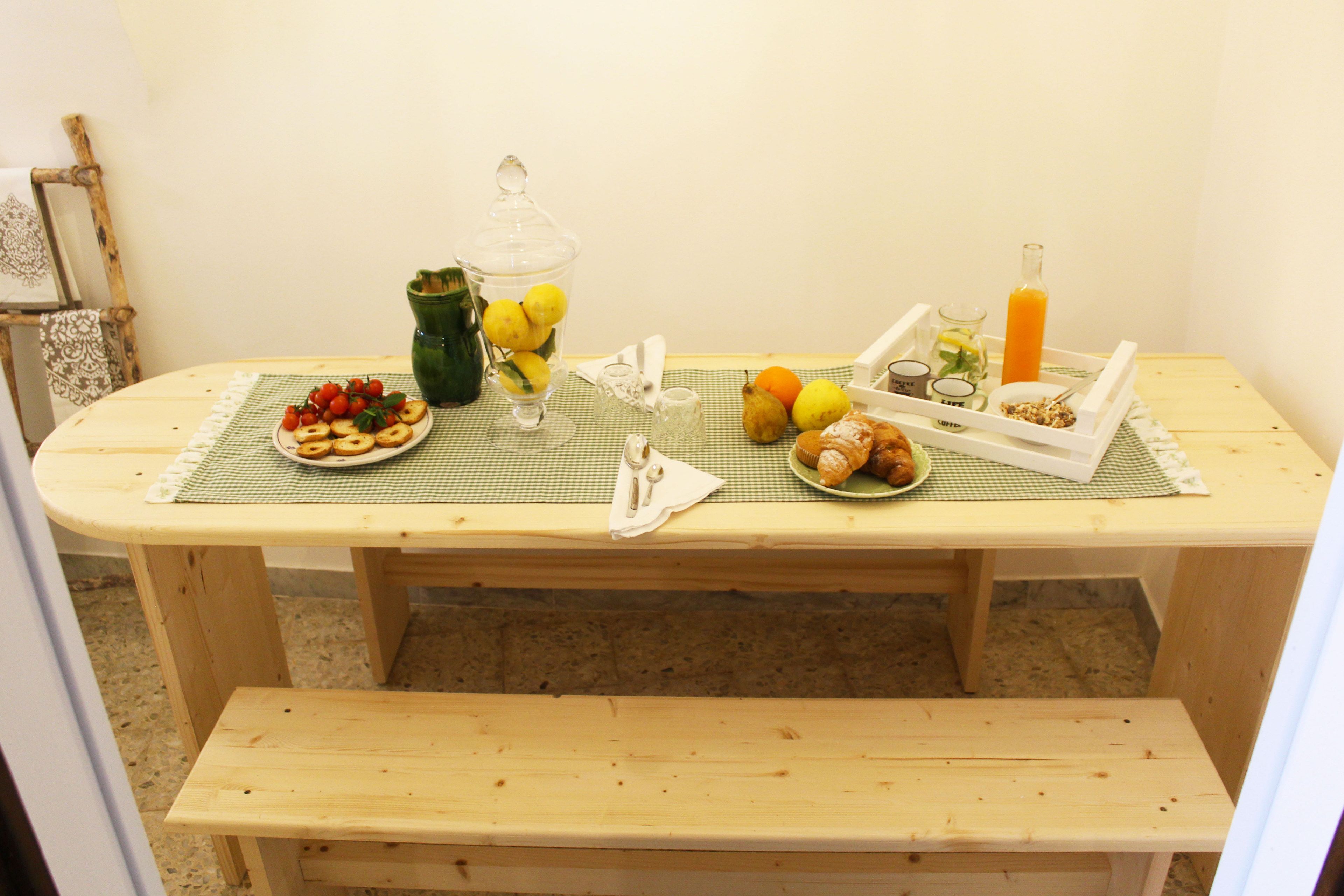 A wooden table with a checkered placemat, a glass jar with lemons, a plate of strawberries, a glass of orange juice, and a bottle of orange juice.