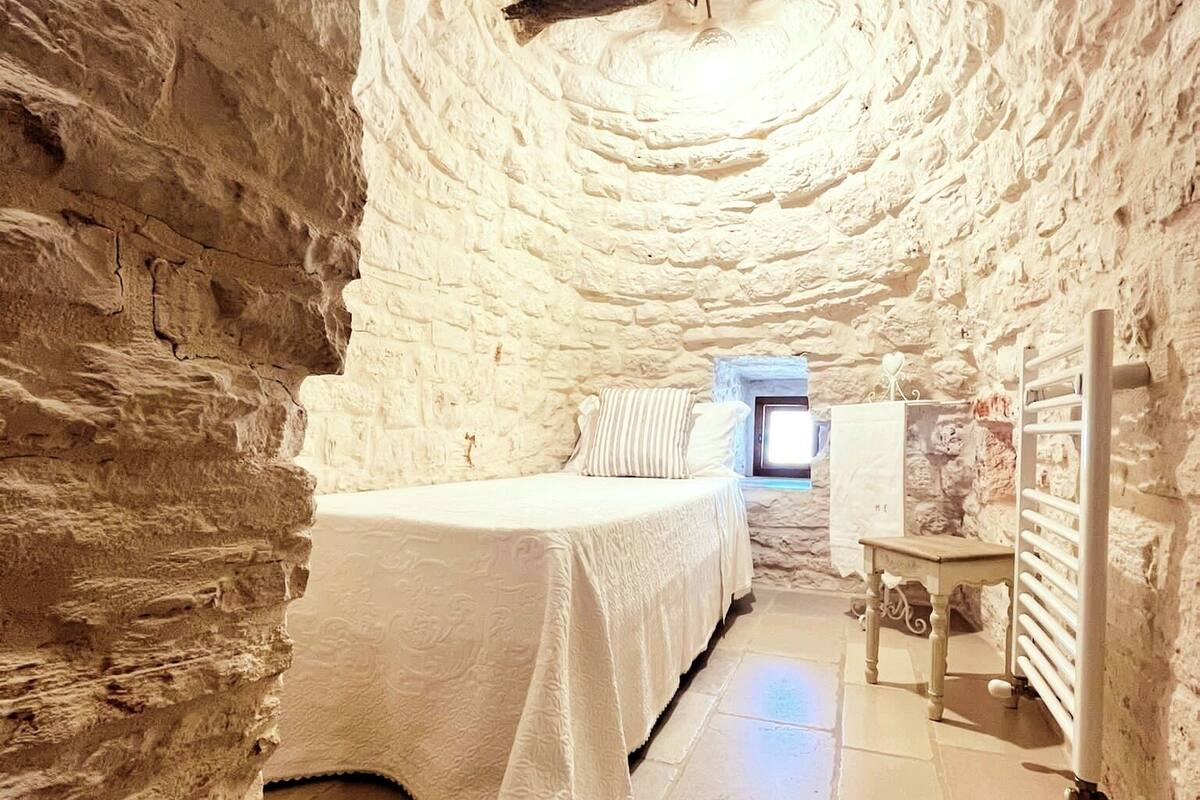Un interior rústico de piedra con una cama, una mesita y un radiador.
