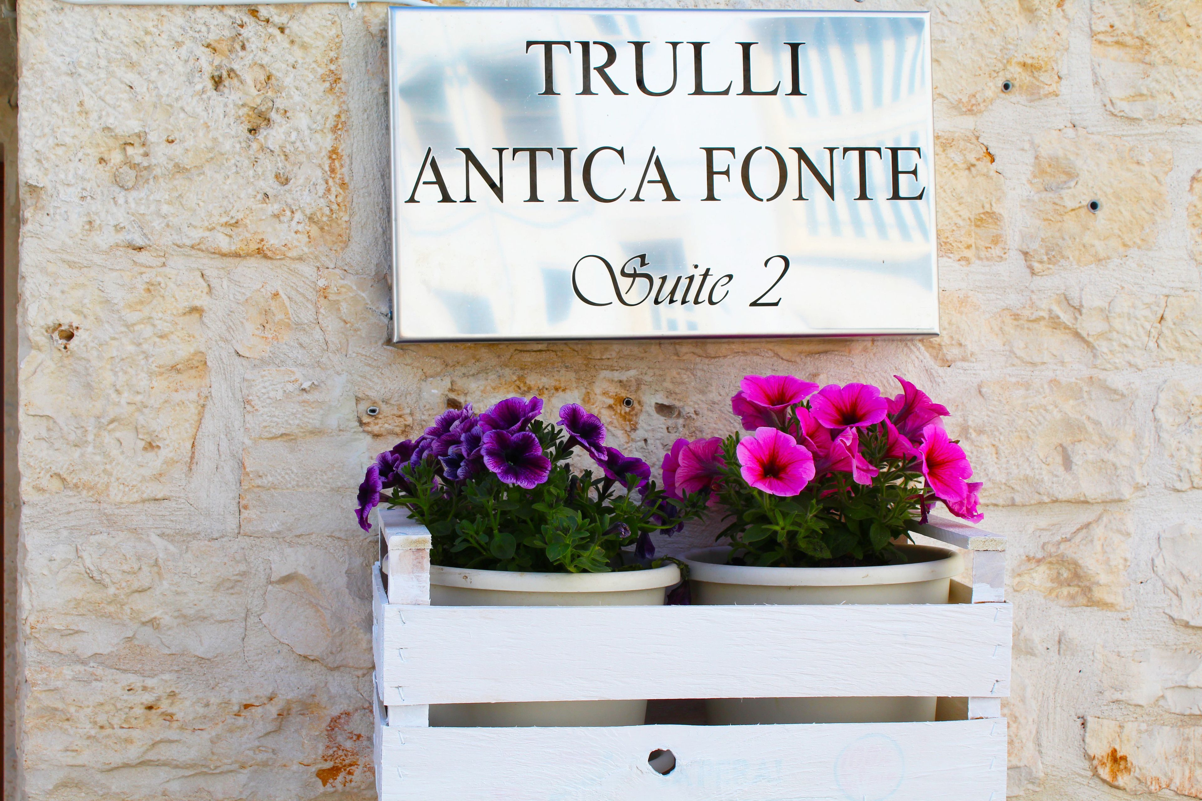 A sign for "Trulli Antica Fonte Suite 2" with two flower planters below it.