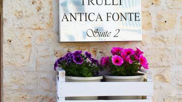 A sign for "Trulli Antica Fonte Suite 2" with two flower planters below it.