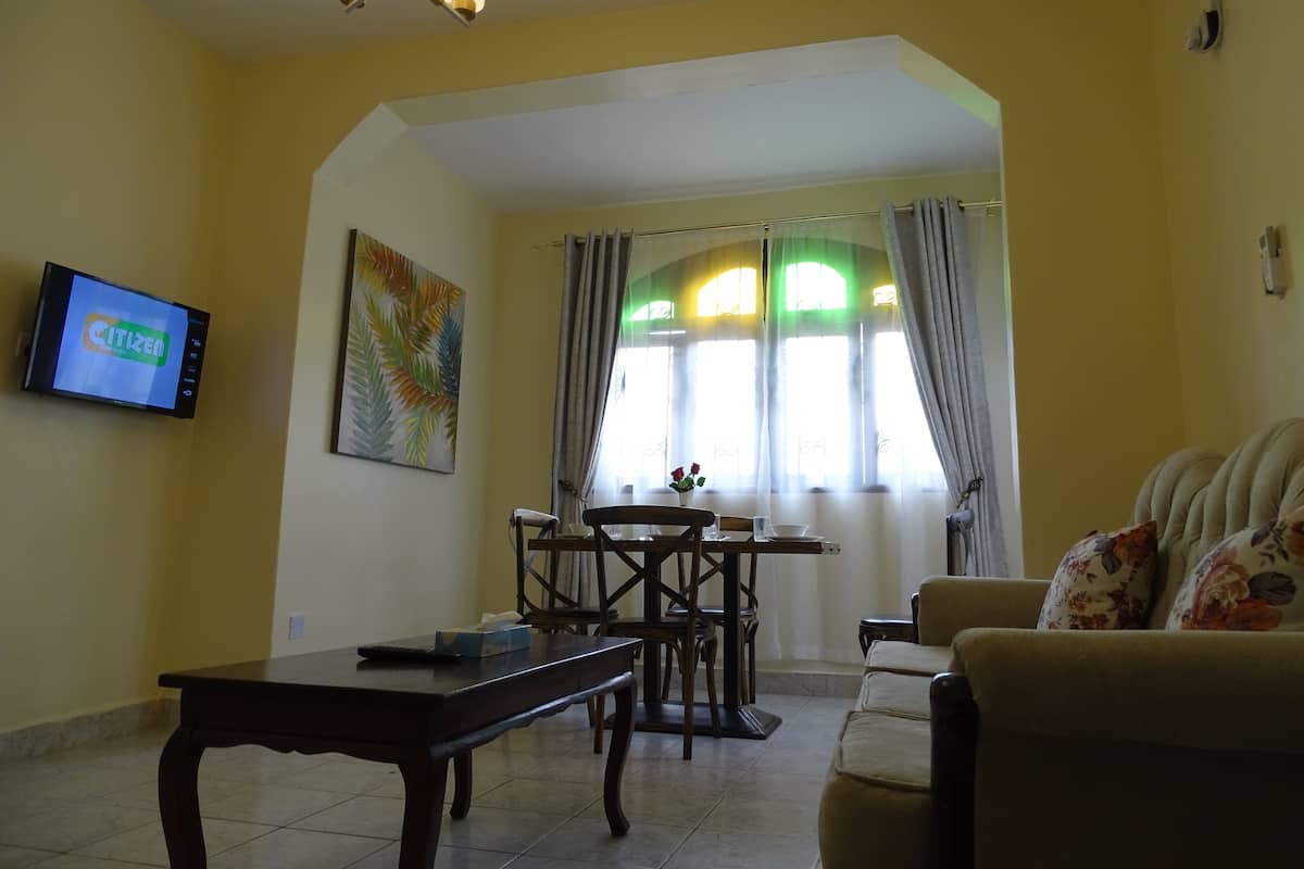 A living room with a dining area, a television mounted on the wall, and a window with curtains.