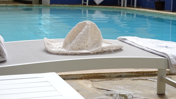 A poolside area with a white lounge chair, a towel, and a decorative hat on the chair. - Nyali Parkside Resort (Mombasa)