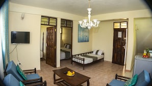 A living room with a sofa set, a dining table with fruit, a TV mounted on the wall, and a chandelier. - Nyali Parkside Resort (Mombasa)