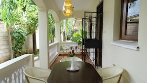 A balcony with a round table and chairs, a hanging light fixture, and a view of a garden. - Nyali Parkside Resort (Mombasa)