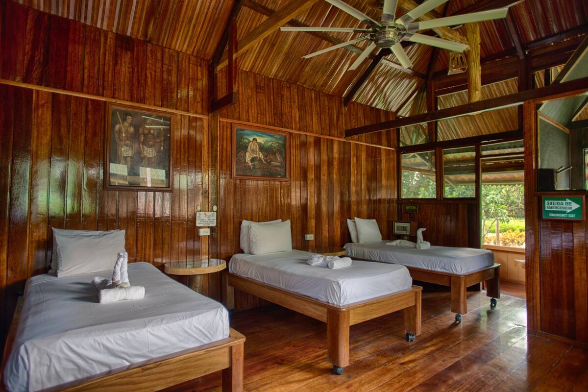 A wooden room with two beds, a ceiling fan, and framed pictures on the walls.