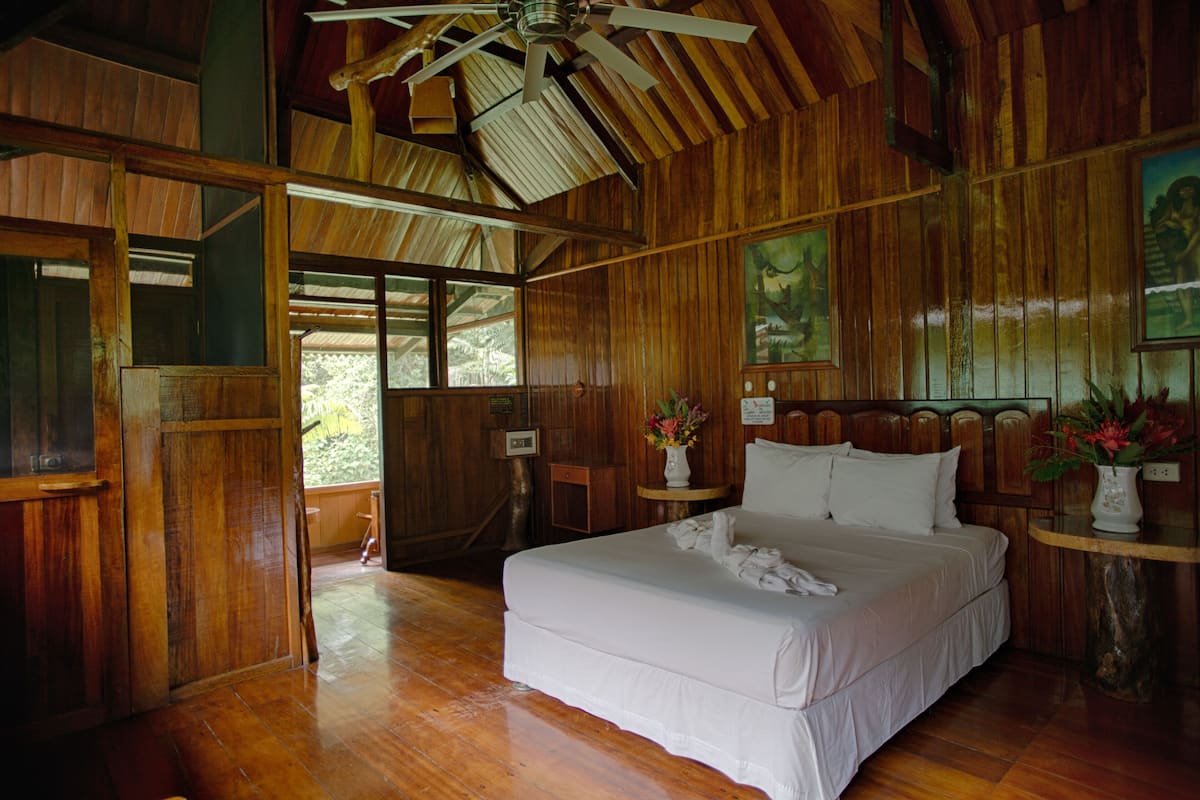 A wooden cabin bedroom with a large bed, wooden walls, and a ceiling fan.