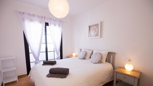 A neatly arranged bedroom with a large bed, bedside lamps, a nightstand, and a window with curtains.