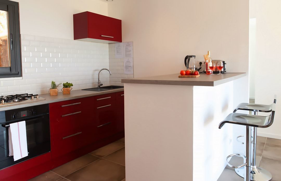 A modern kitchen with red cabinets, a white tiled backsplash, a gas stove, and a small island with bar stools.