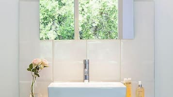 Een badkamer met een wit wastafelmeubel, houten opbergruimte en een raam met uitzicht op groen.