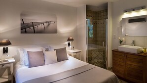 Een moderne hotelkamer met een groot bed, nachtlampjes, een badkamer met een wastafel en spiegel, en een douchehoek.