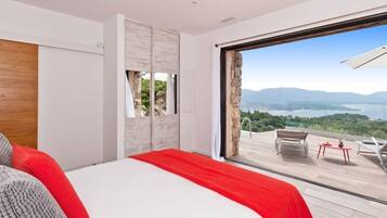 A bedroom with a large bed, a view of a balcony with outdoor furniture, and a stone wall.