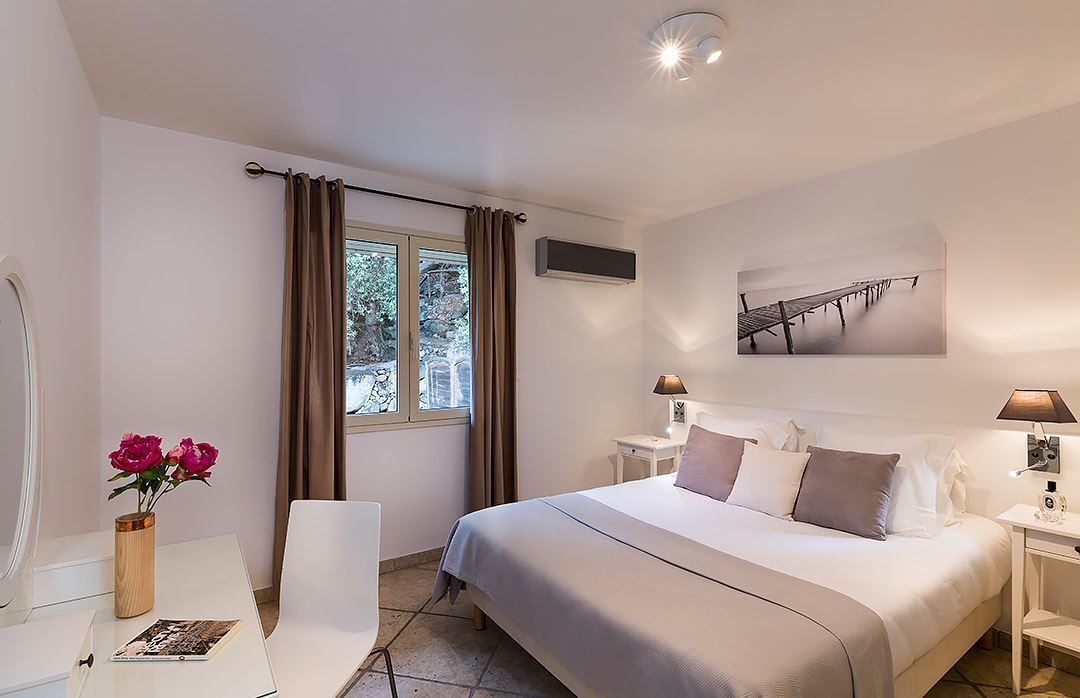 Habitación de hotel con cama, mesitas de noche, escritorio, silla, ventana con cortinas, aire acondicionado de pared y un cuadro enmarcado.