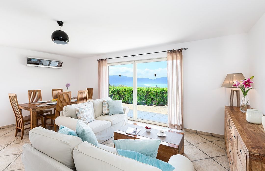Una sala moderna con sofá, mesa de centro y comedor. Hay un ventanal con vistas a zonas verdes y montañas.