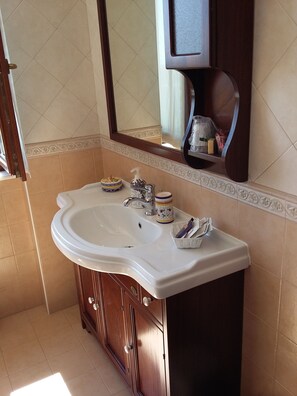 A bathroom with a white sink, wooden cabinets, a mirror, and a shelf with toiletries. - Postiglione Country House (Cingoli)