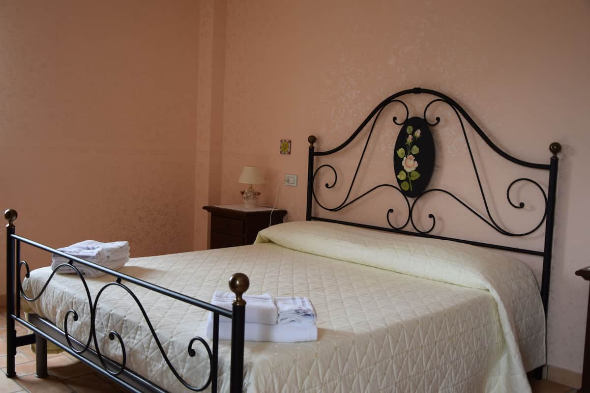 A neatly made bed with a quilted white bedspread, a decorative headboard with a floral design, and a small bedside table with a lamp.