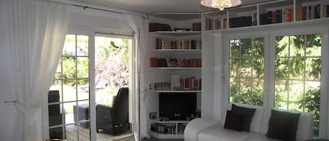 A modern living room with a white sofa, a bookshelf, and a dining area with a table and chairs.