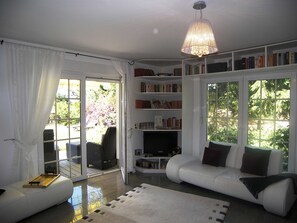 Een moderne woonkamer met een witte bank, een boekenkast en een eethoek met een tafel en stoelen.