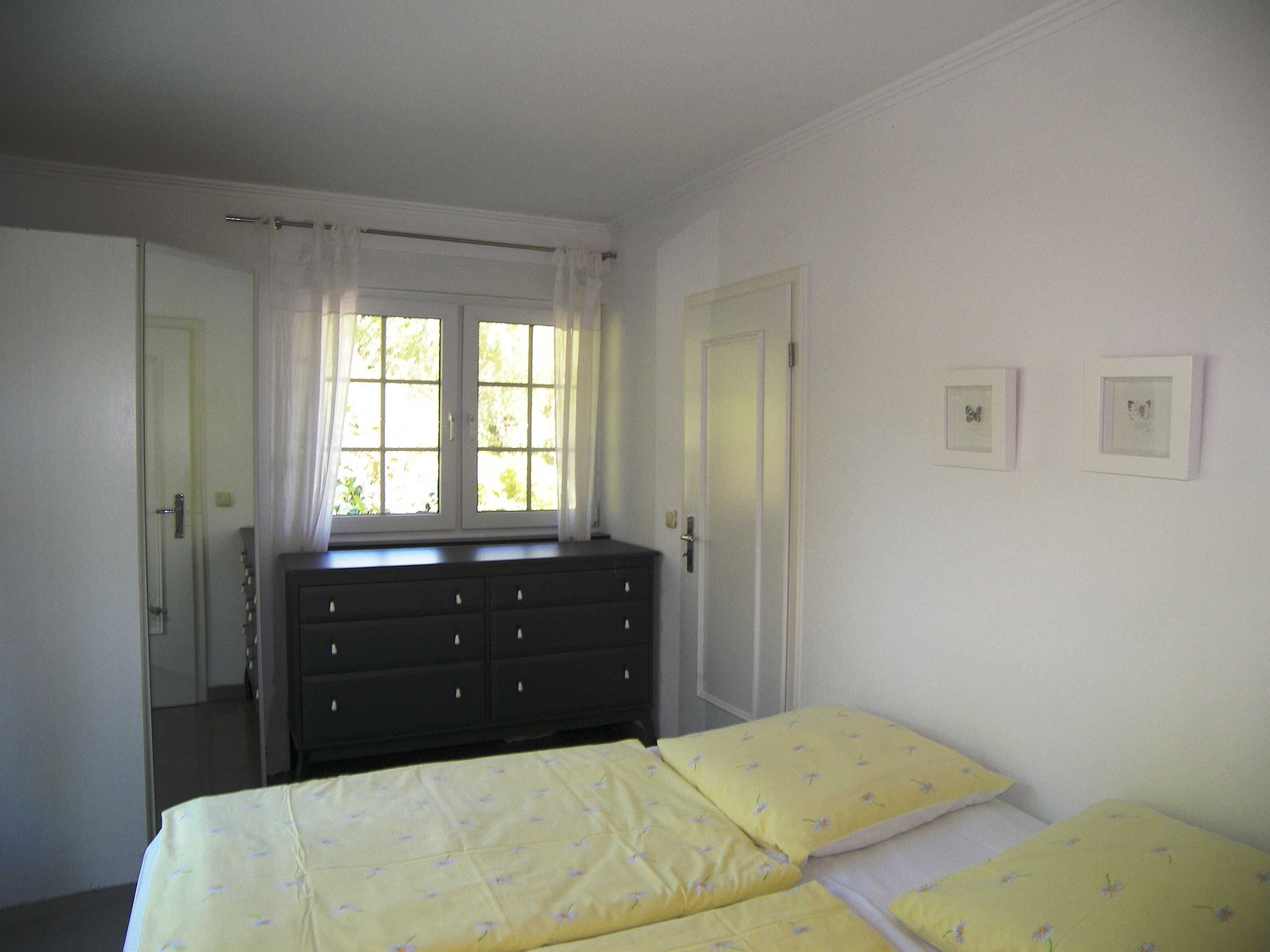 Un dormitorio con cama, cómoda, ventana con cortinas y dos cuadros en la pared.