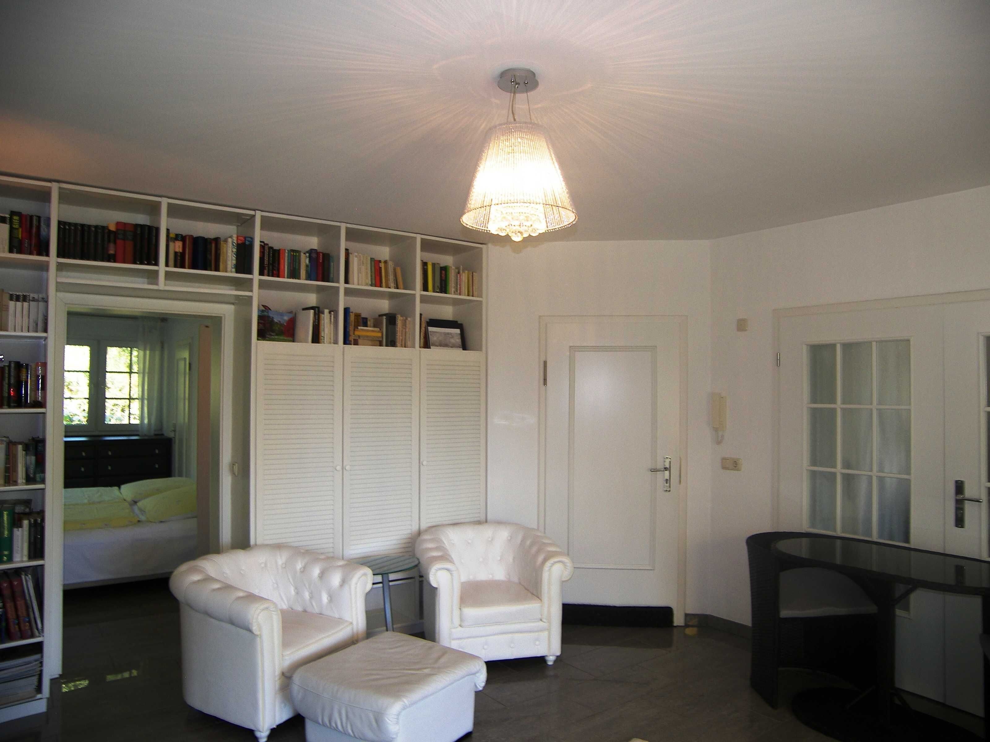 Una habitación con un sillón blanco, un reposapiés a juego, una estantería y una puerta con paneles de vidrio satinado.