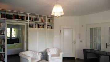 Una habitación con un sillón blanco, un reposapiés a juego, una estantería y una puerta con paneles de vidrio satinado.
