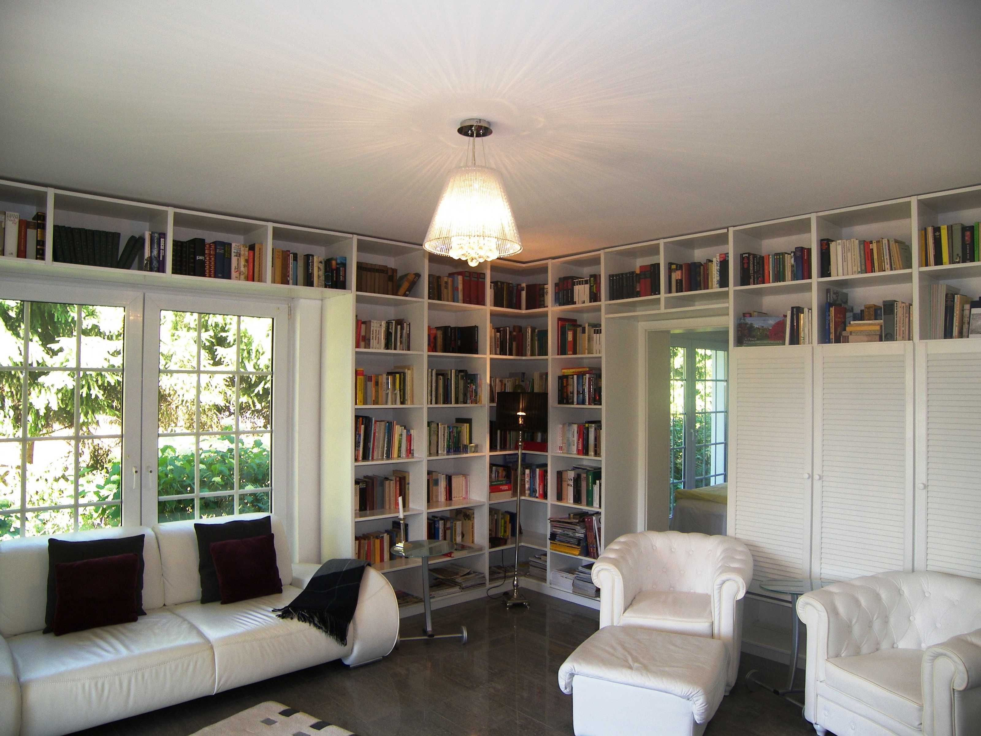 Eine Bibliothek mit weißen Regalen voller Bücher, einem weißen Sofa und einem weißen Sessel.