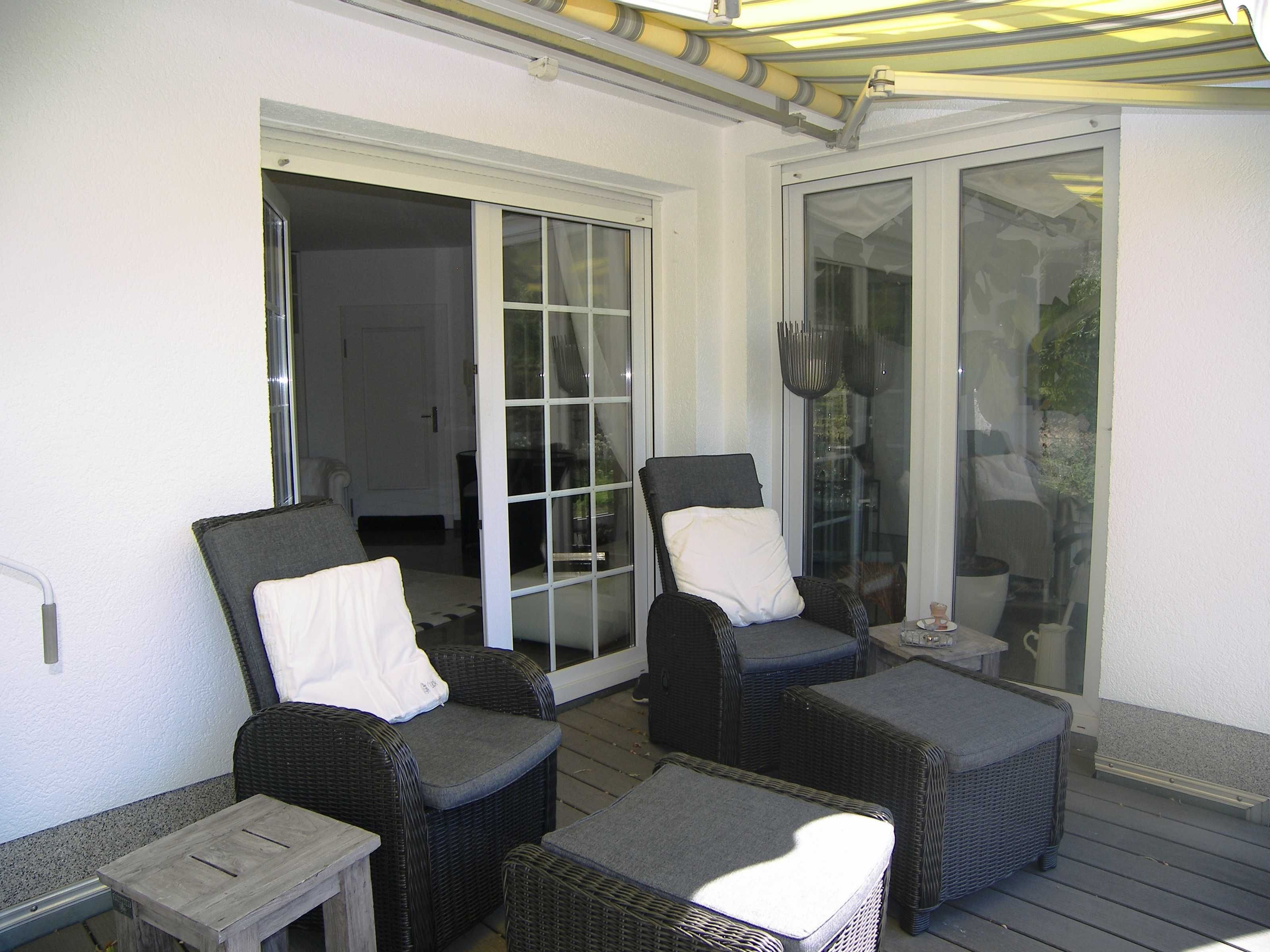 Eine überdachte Terrasse mit Korbmöbeln, darunter zwei Stühle und ein kleiner Tisch.