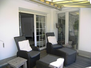 Een overdekt terras met rieten meubels, waaronder twee stoelen en een bijzettafeltje.